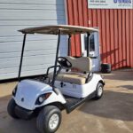 White 2011 Yamaha Drive Gas Golf Car that's for sale. The golf car is in front of Northern Hill Golf Car with a light red and white exterior.